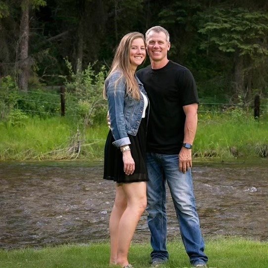Photograph of Quentin and Ashley the owners of a local family run custom home building company standing together next to a beautiful mountain river in the East Kootenays.
